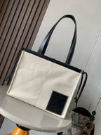 Cream canvas tote bag with dark leather handles and front logo patch
