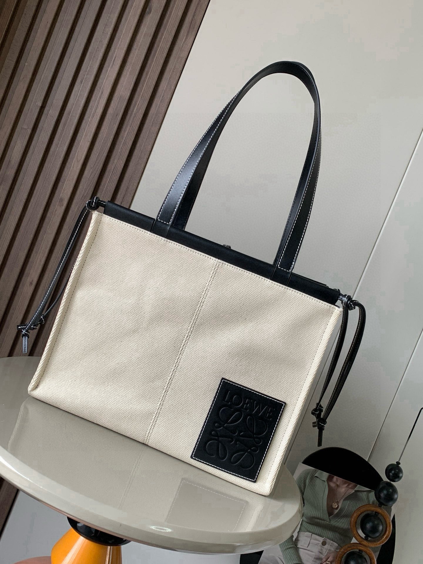 Cream canvas tote bag with dark leather handles and front logo patch