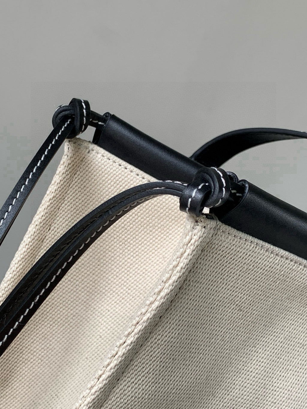 Cream canvas and black leather tote bag close-up of top handle loop