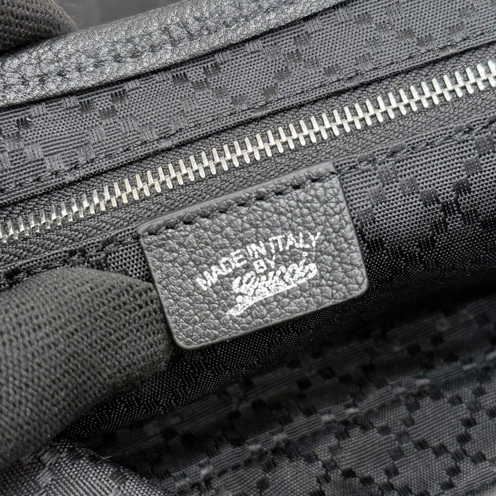 Gucci bag label with “MADE IN ITALY” on dark jacquard fabric near zipper