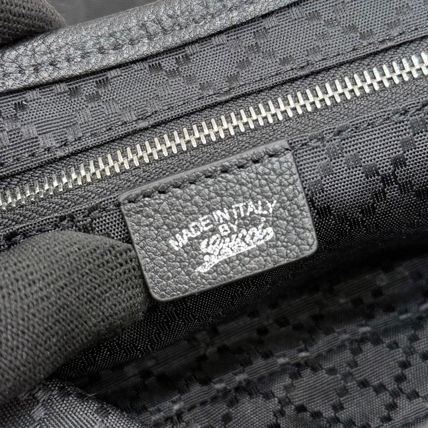 Gucci bag label with “MADE IN ITALY” on dark jacquard fabric near zipper