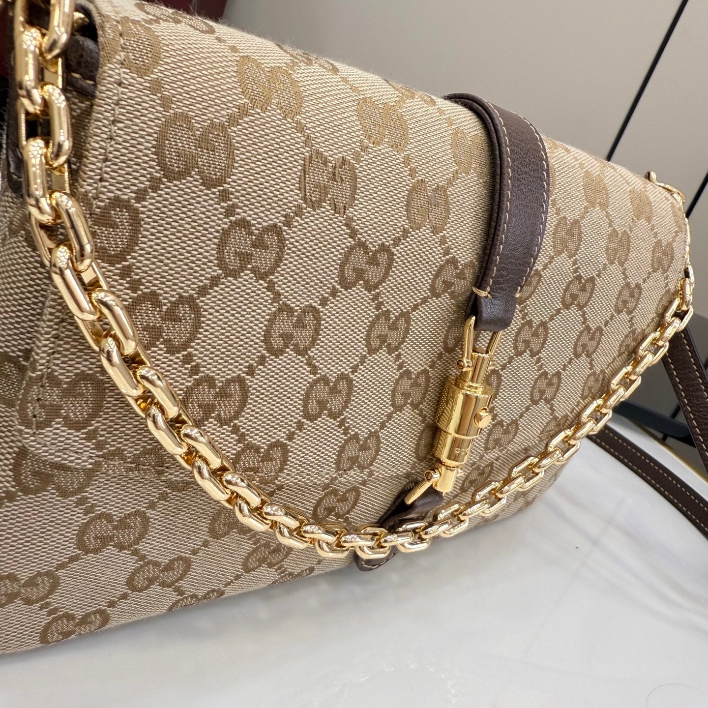 Gucci bag with beige GG-print canvas, dark brown leather strap, and gold chain handle.