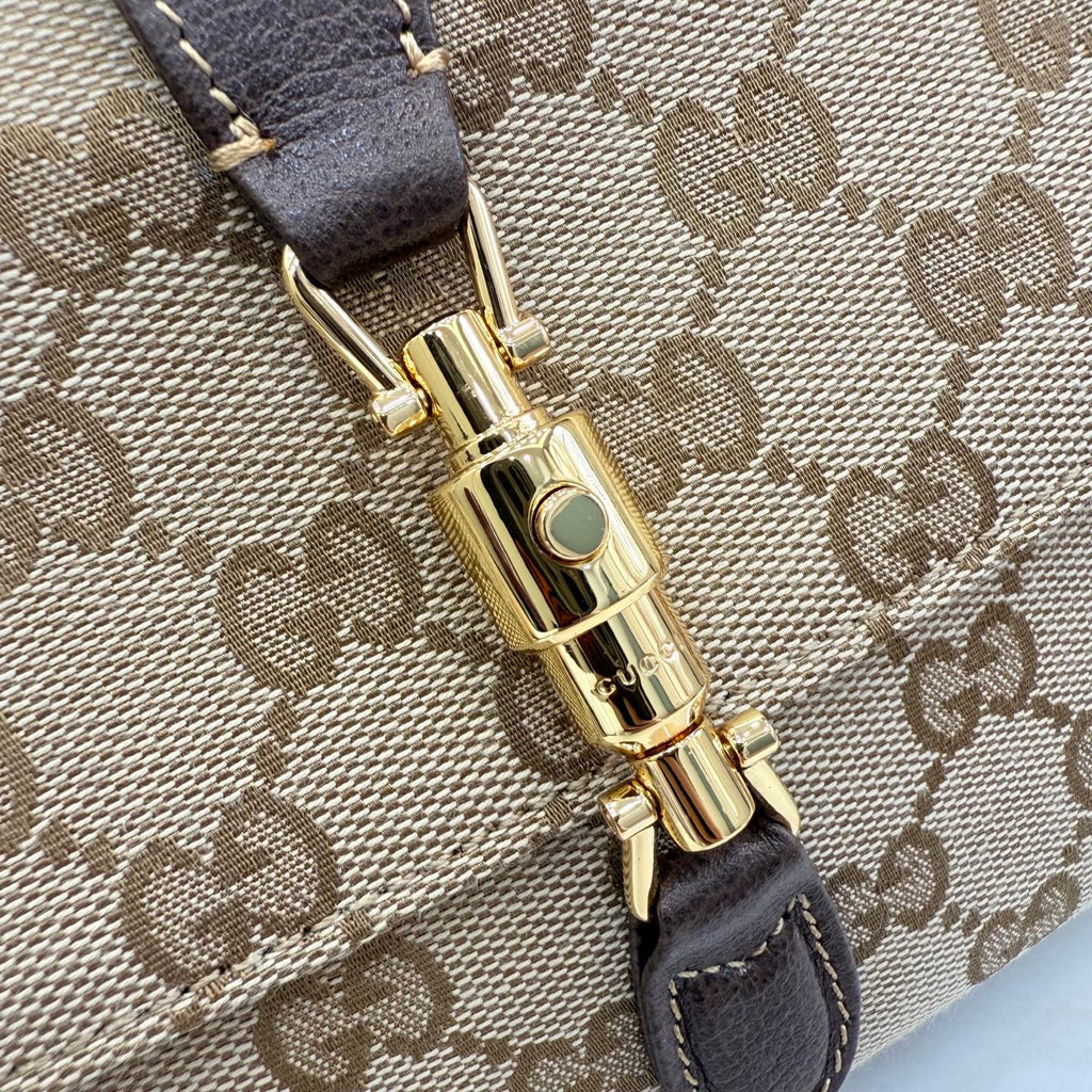 Gold-tone clasp with green accent on brown leather and beige GG canvas shoulder bag
