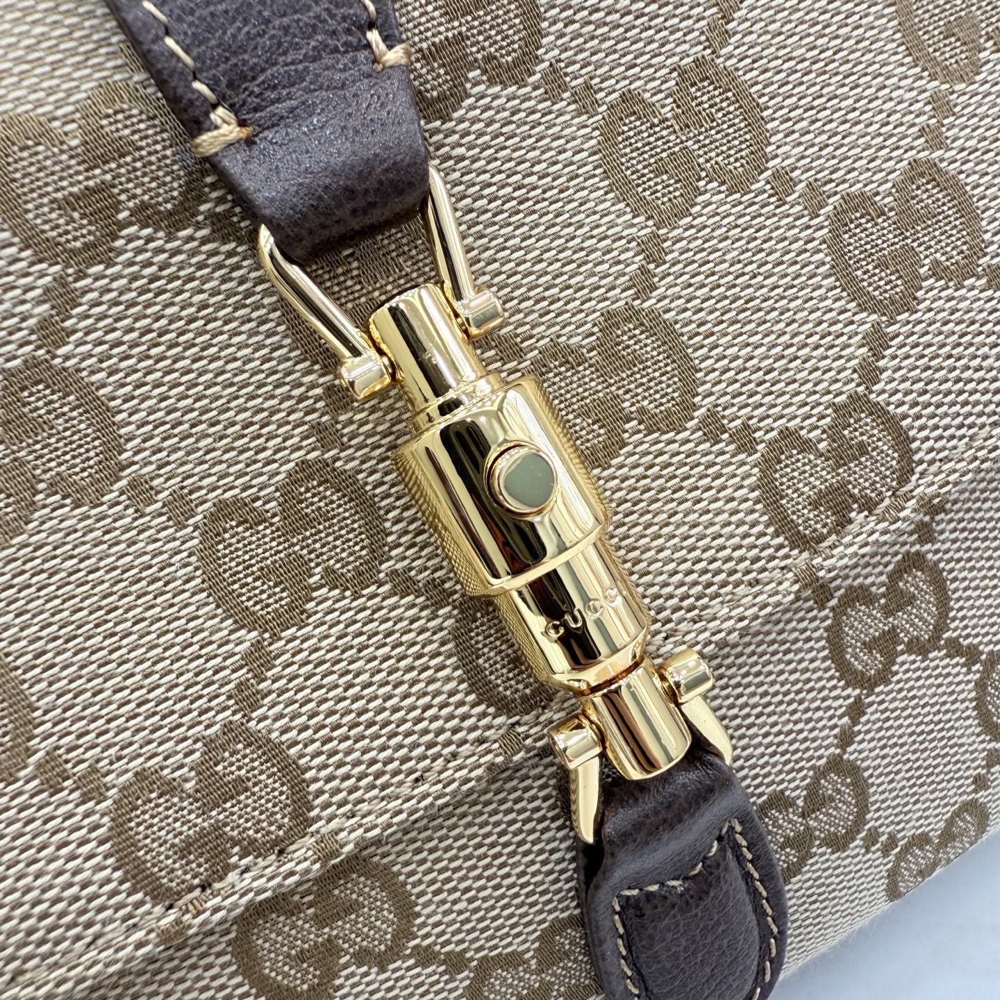 Gold-tone clasp with green accent on brown leather and beige GG canvas shoulder bag