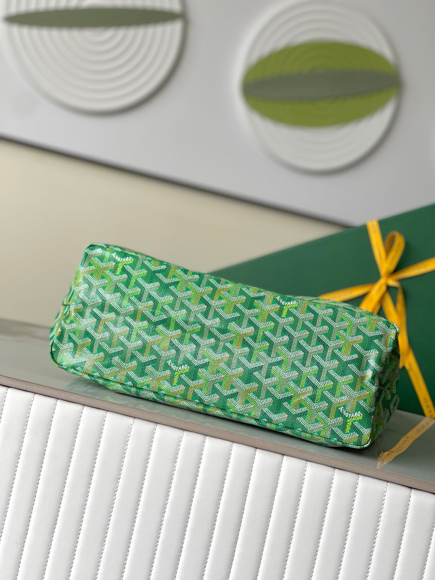 Green patterned clutch-style handbag with zipper top and gold ribbon detail