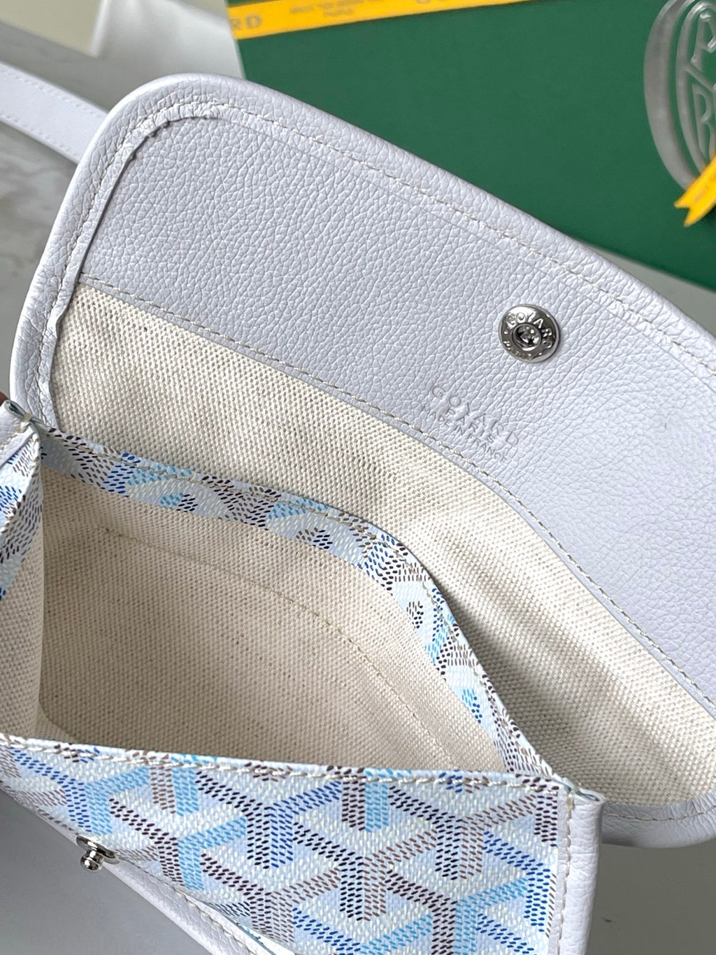 White fabric-lined interior pocket in a light blue and white Goyard-pattern bag.