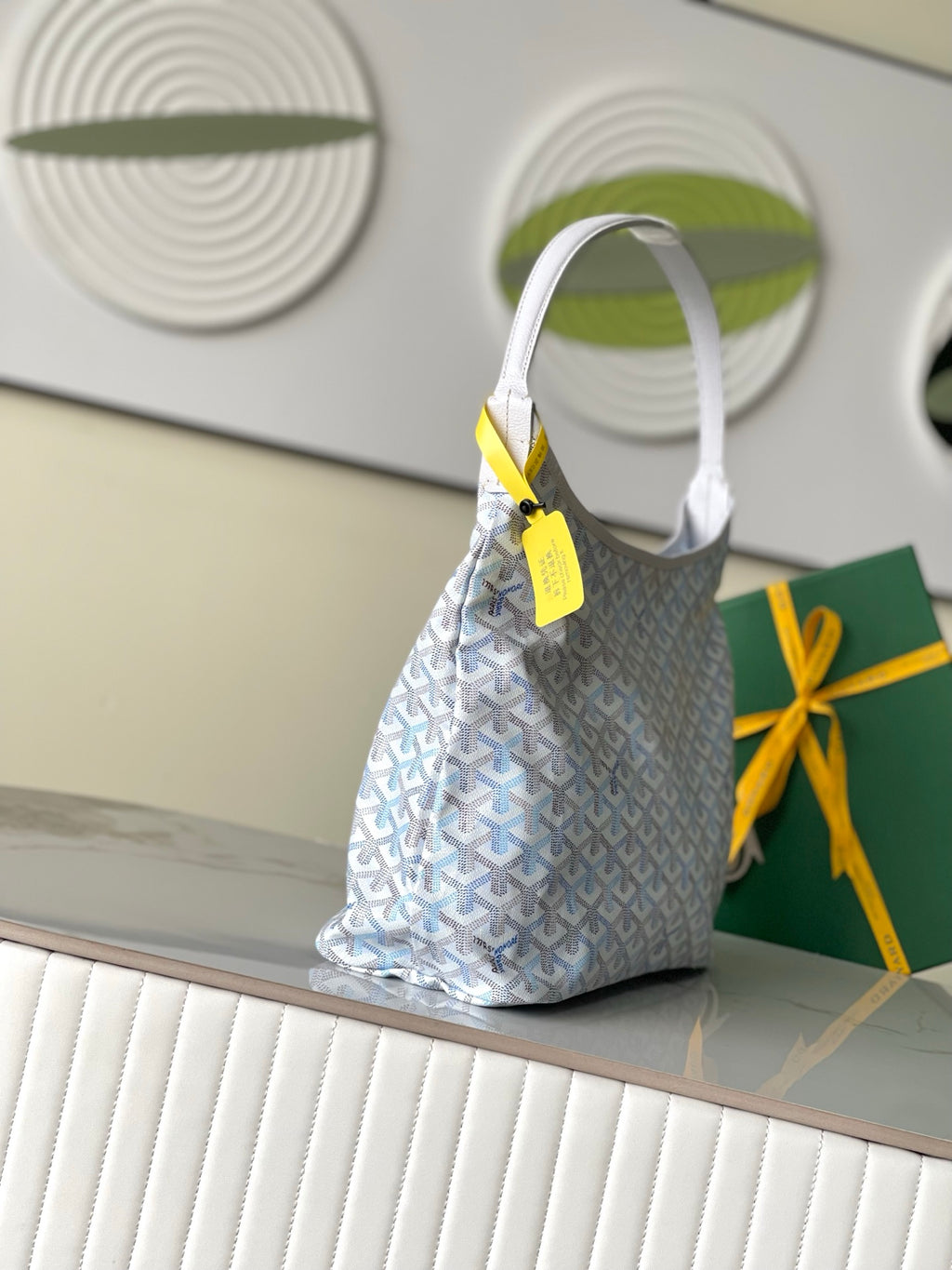 Light blue and white Goyard-pattern hobo bag with top handle and front yellow tag.