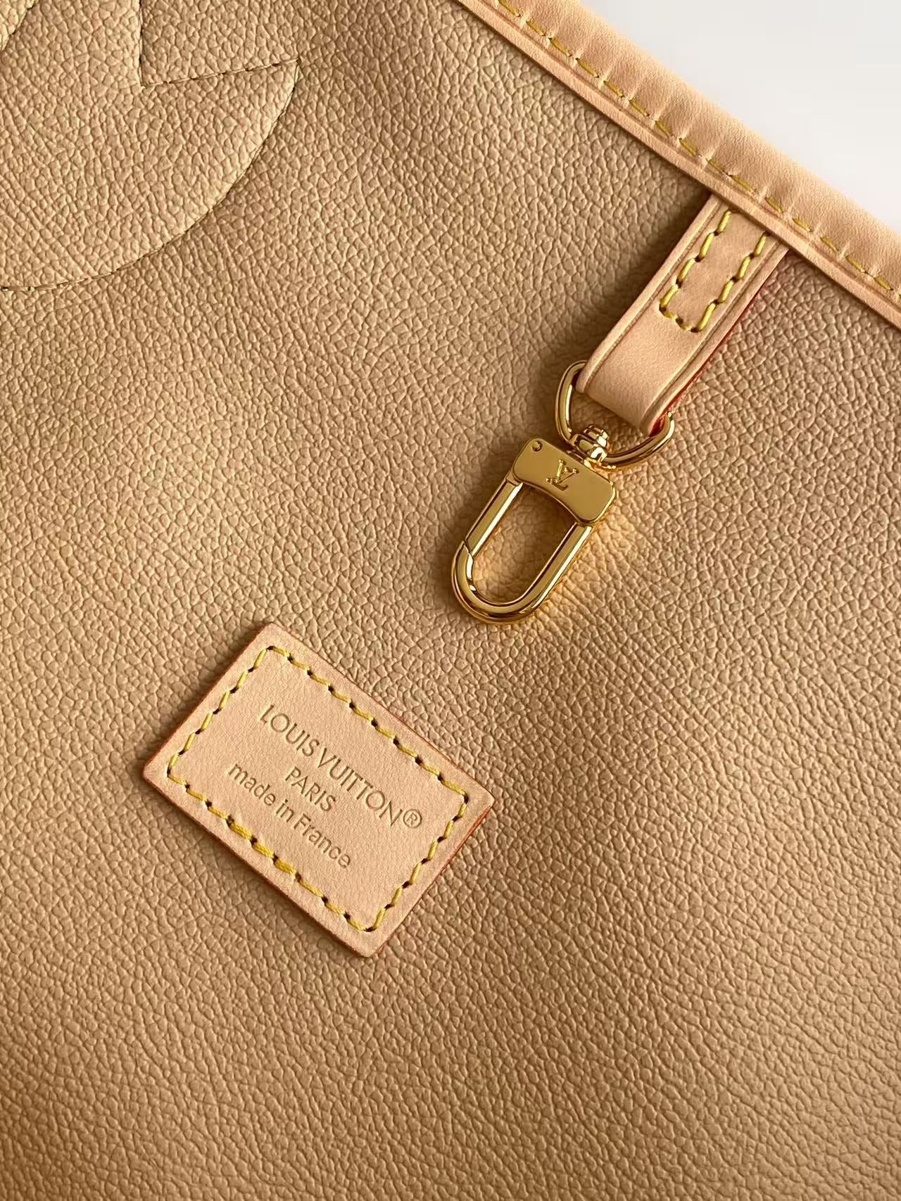 Louis Vuitton leather label and gold-tone clasp on tan bag interior