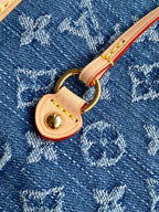 Close-up of blue monogram bag with tan leather pull tab and gold-tone ring