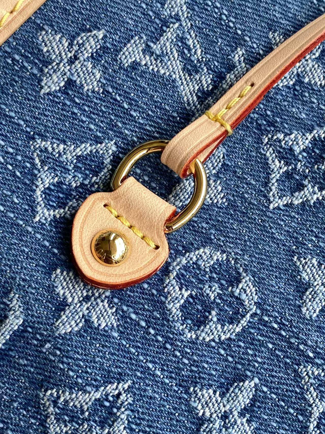 Close-up of blue monogram bag with tan leather pull tab and gold-tone ring