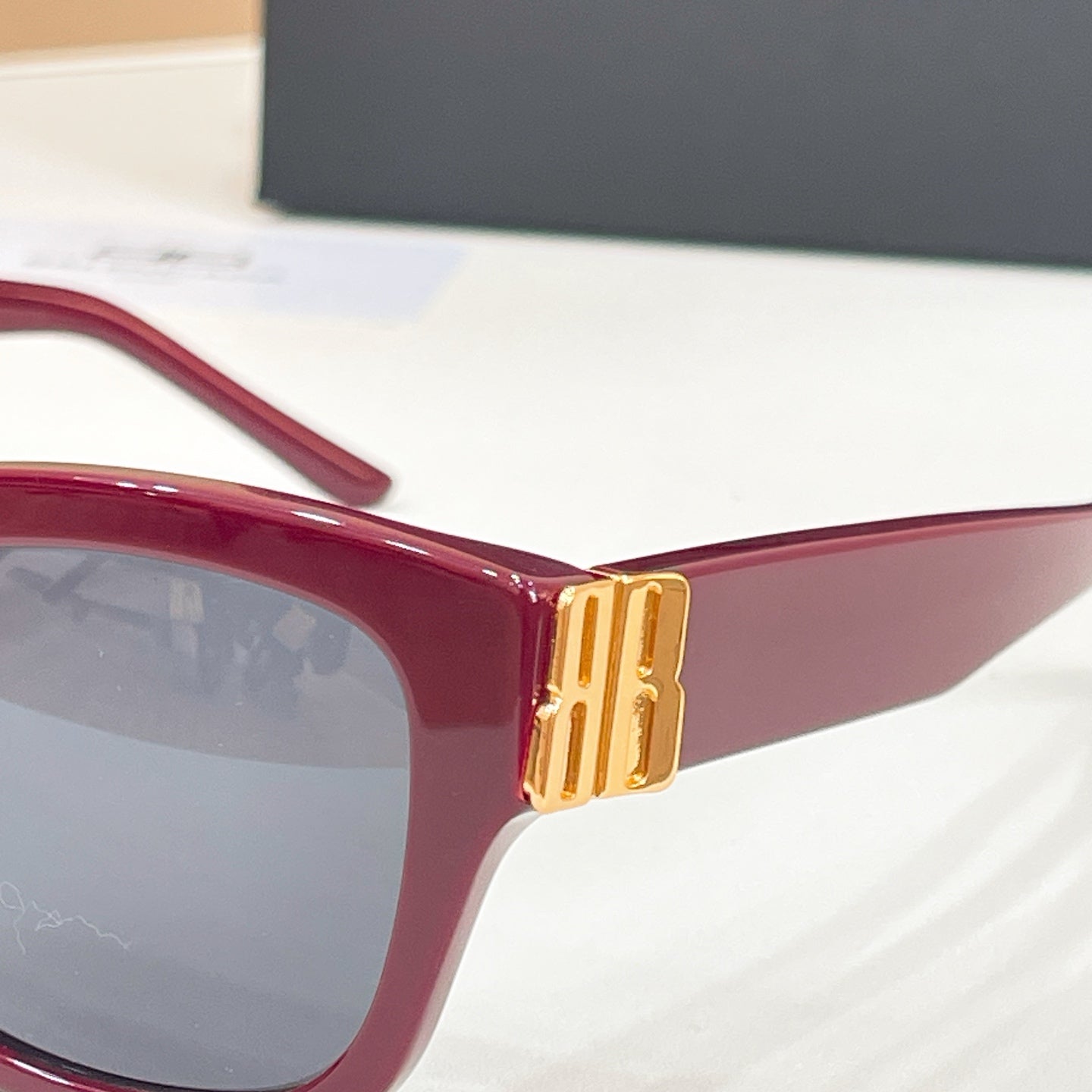 Close-up red square sunglasses with gold logo temple hinge and tinted lens