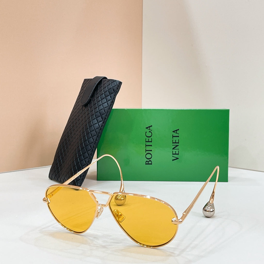 Gold-tone sunglasses with yellow-tinted lenses on a display stand