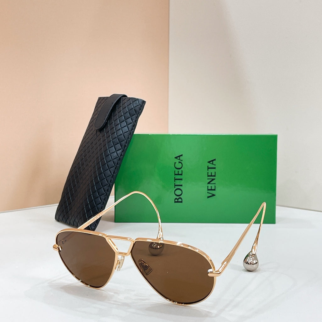 Gold-tone sunglasses with dark brown-tinted lenses on a display stand