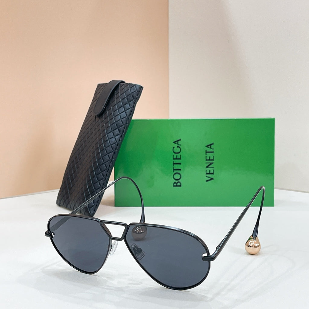 Black aviator sunglasses with dark lenses and gold-tone trim, placed with a black case