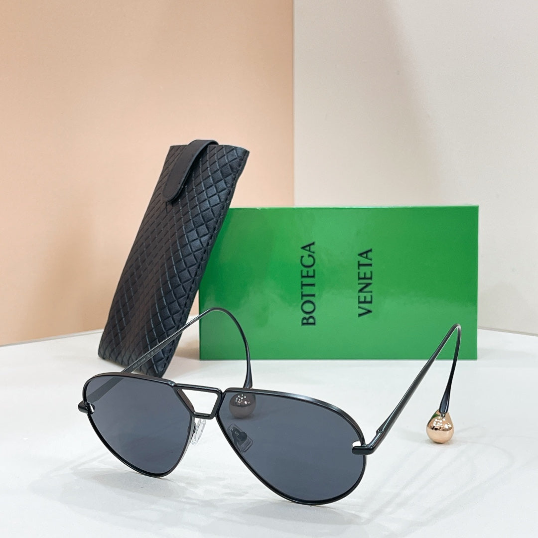 Black aviator sunglasses with dark lenses and gold-tone trim, placed with a black case