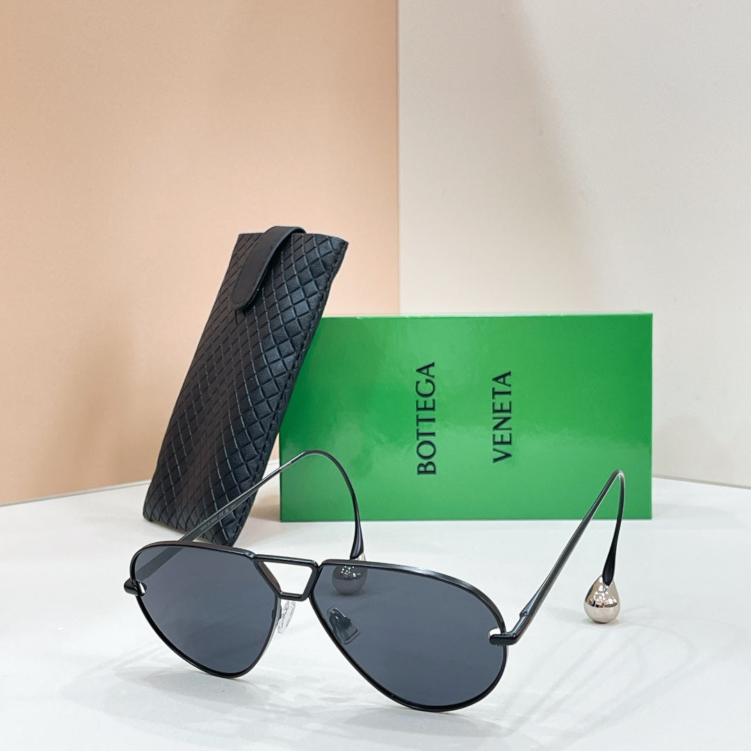 Black aviator sunglasses with dark lenses and gold-tone trim, beside a black case