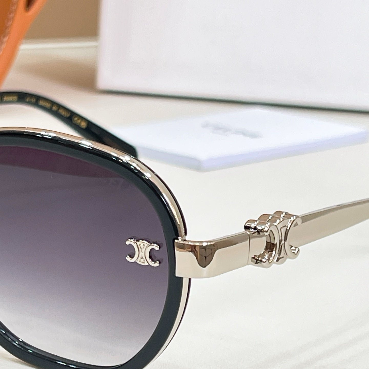 Close-up of round sunglasses with dark lens and gold-tone temple logo emblem