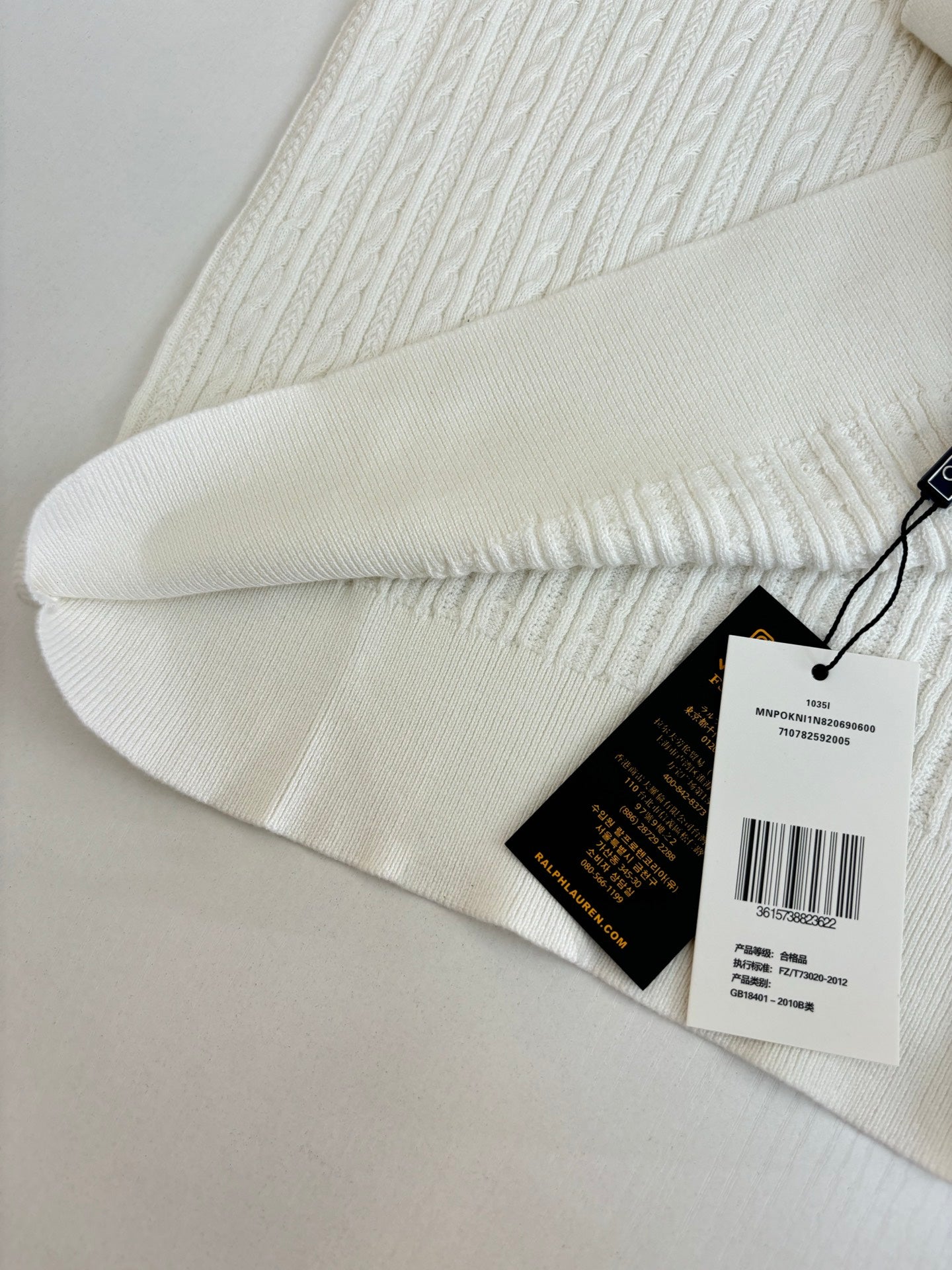 White cable-knit polo shirt sleeve hem with product hang tags