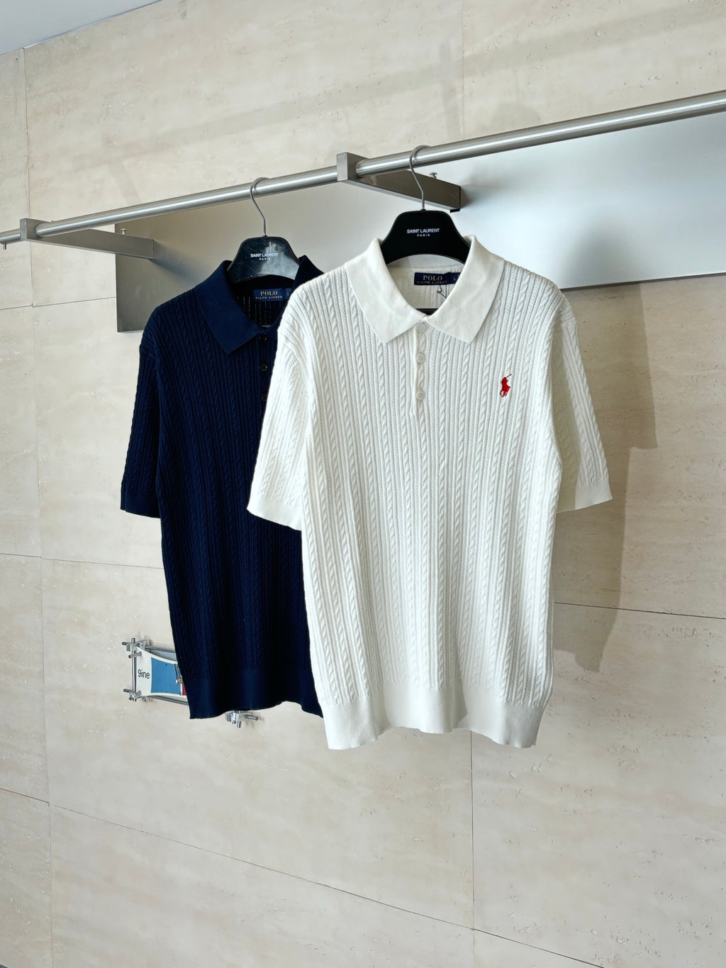 White cable-knit polo shirt with short sleeves and red logo, on hanger