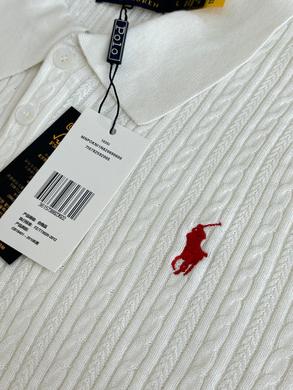 White cable-knit polo shirt with small red logo and attached hang tags