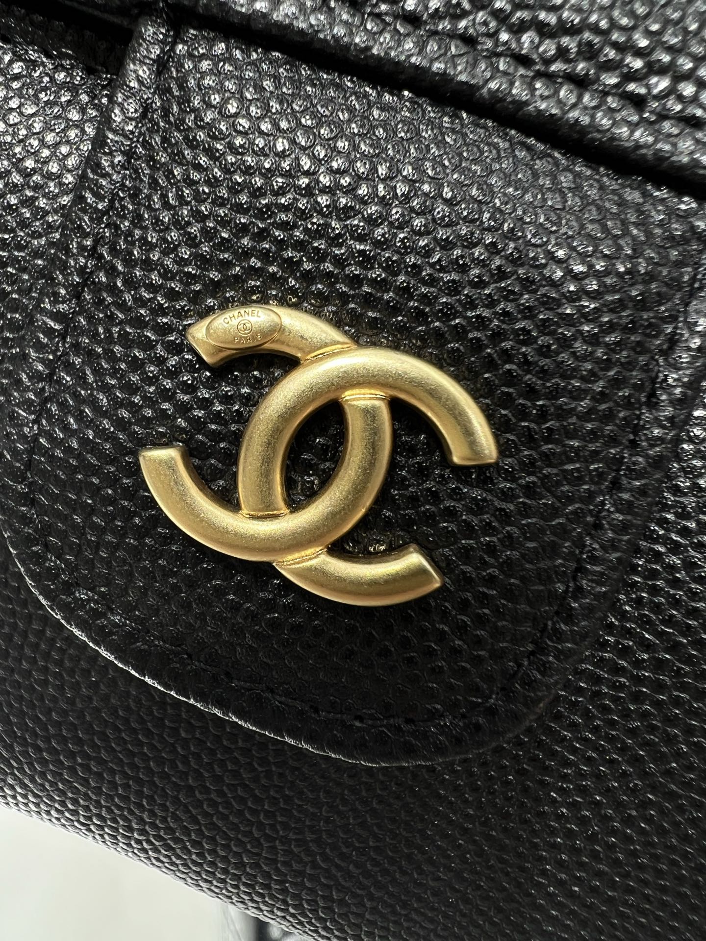Black Chanel bag close-up of gold CC logo on textured leather flap.