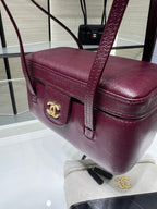 Burgundy Chanel bag front with gold CC emblem and flap clasp, leather top