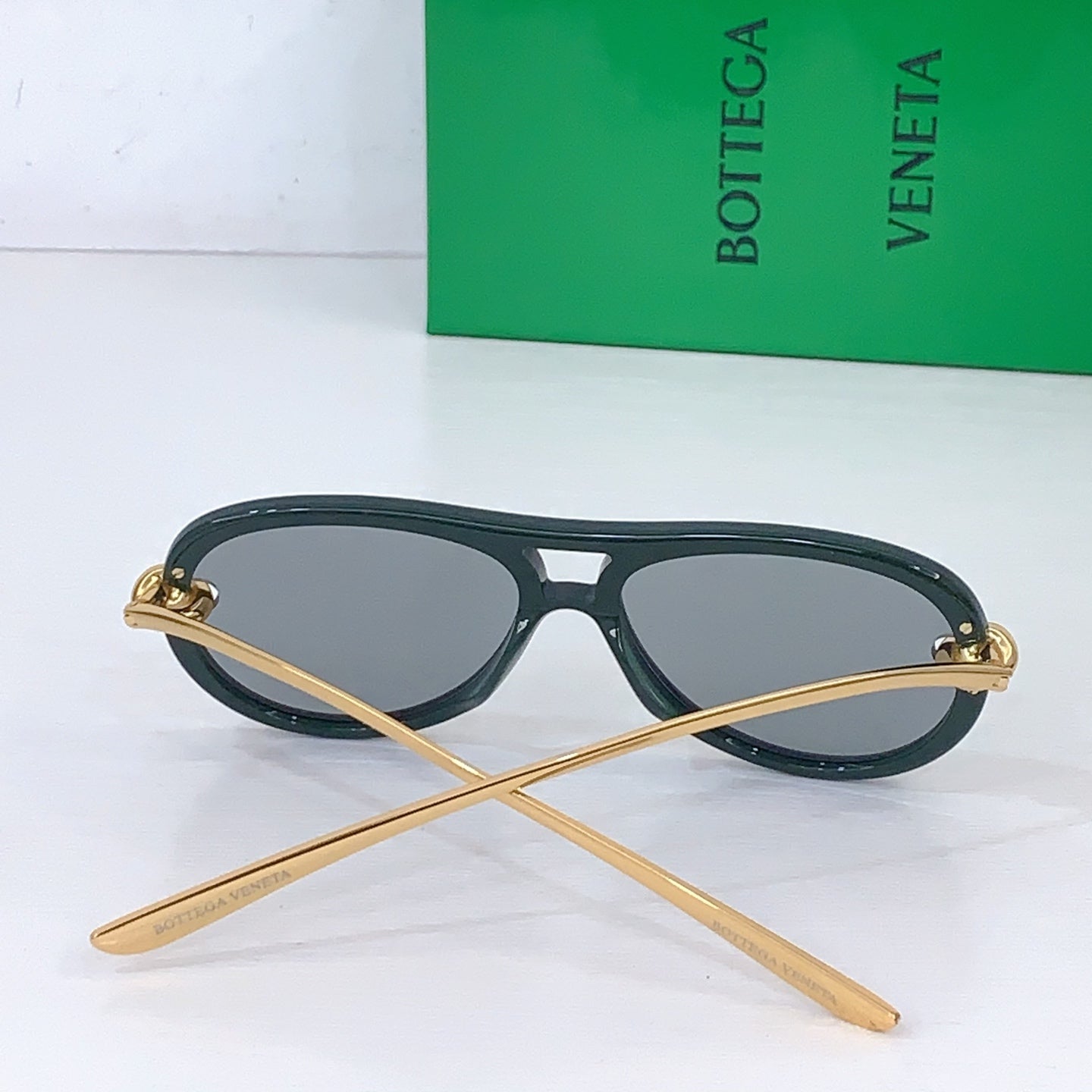 Bottega Veneta sunglasses with dark green frames, gray lenses, and gold-tone temples