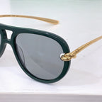 Bottega Veneta sunglasses close-up with dark green frame, gray lenses, and gold hinge