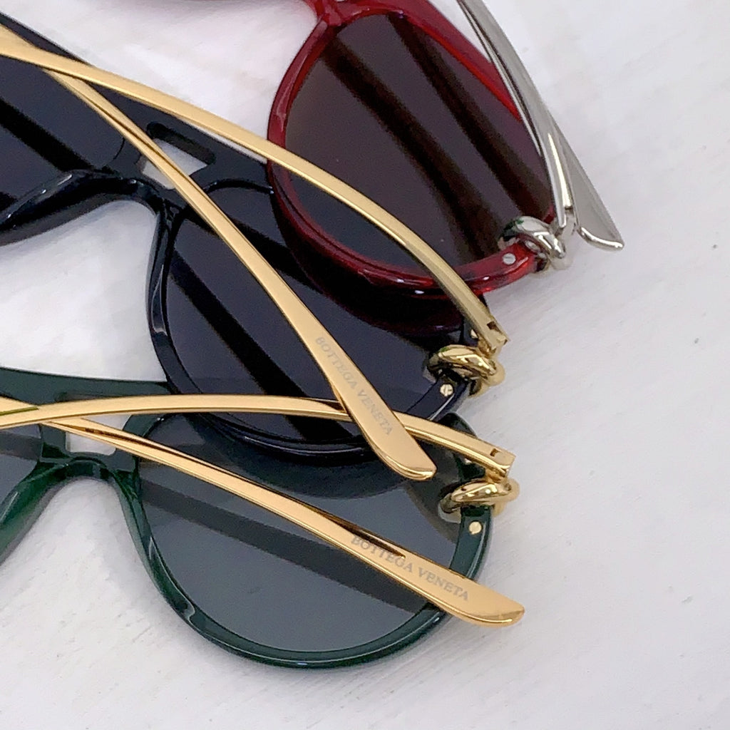 Bottega Veneta sunglasses layered together: black pair and green pair with gold temples