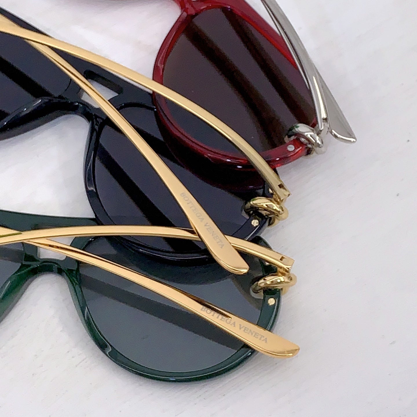 Bottega Veneta sunglasses layered together: black pair and green pair with gold temples