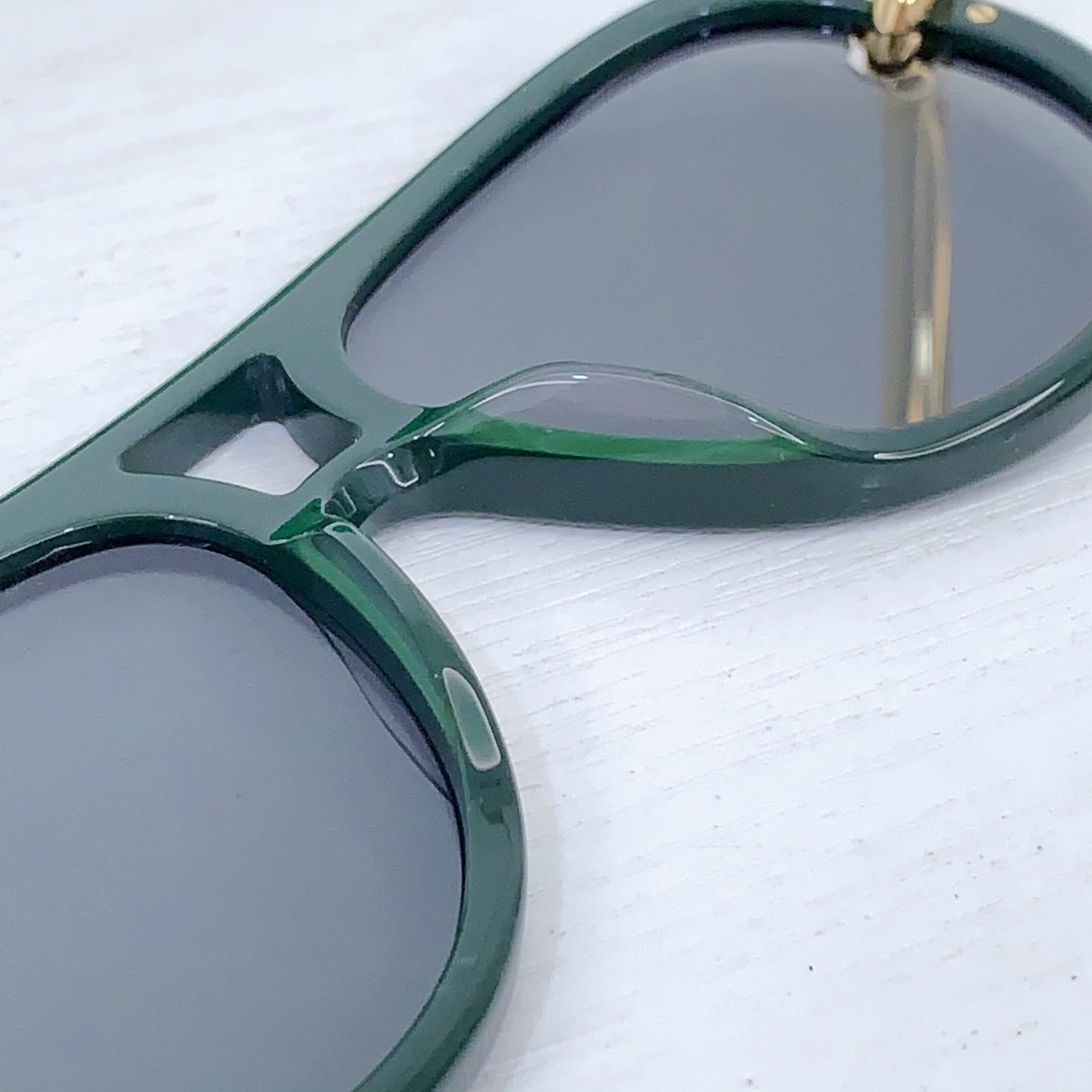 Bottega Veneta sunglasses close-up of dark green frame and gray lens with gold joint