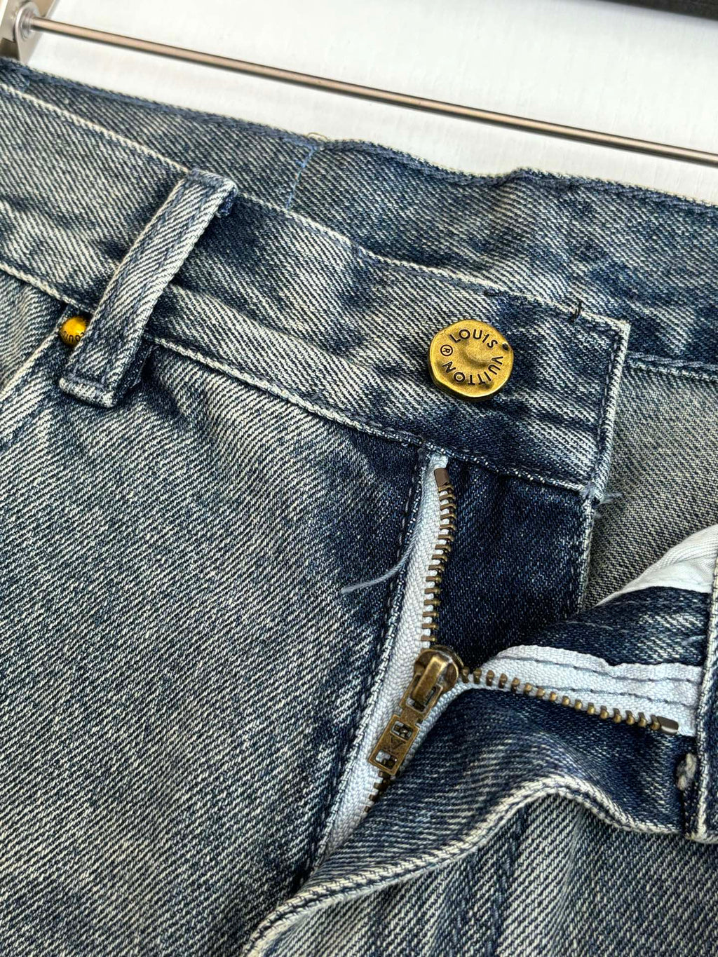 Close-up of denim shorts front with gold-toned button and zipper fly