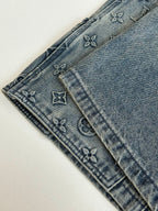 Denim shorts leg close-up with monogram-pattern stitching and belt loops