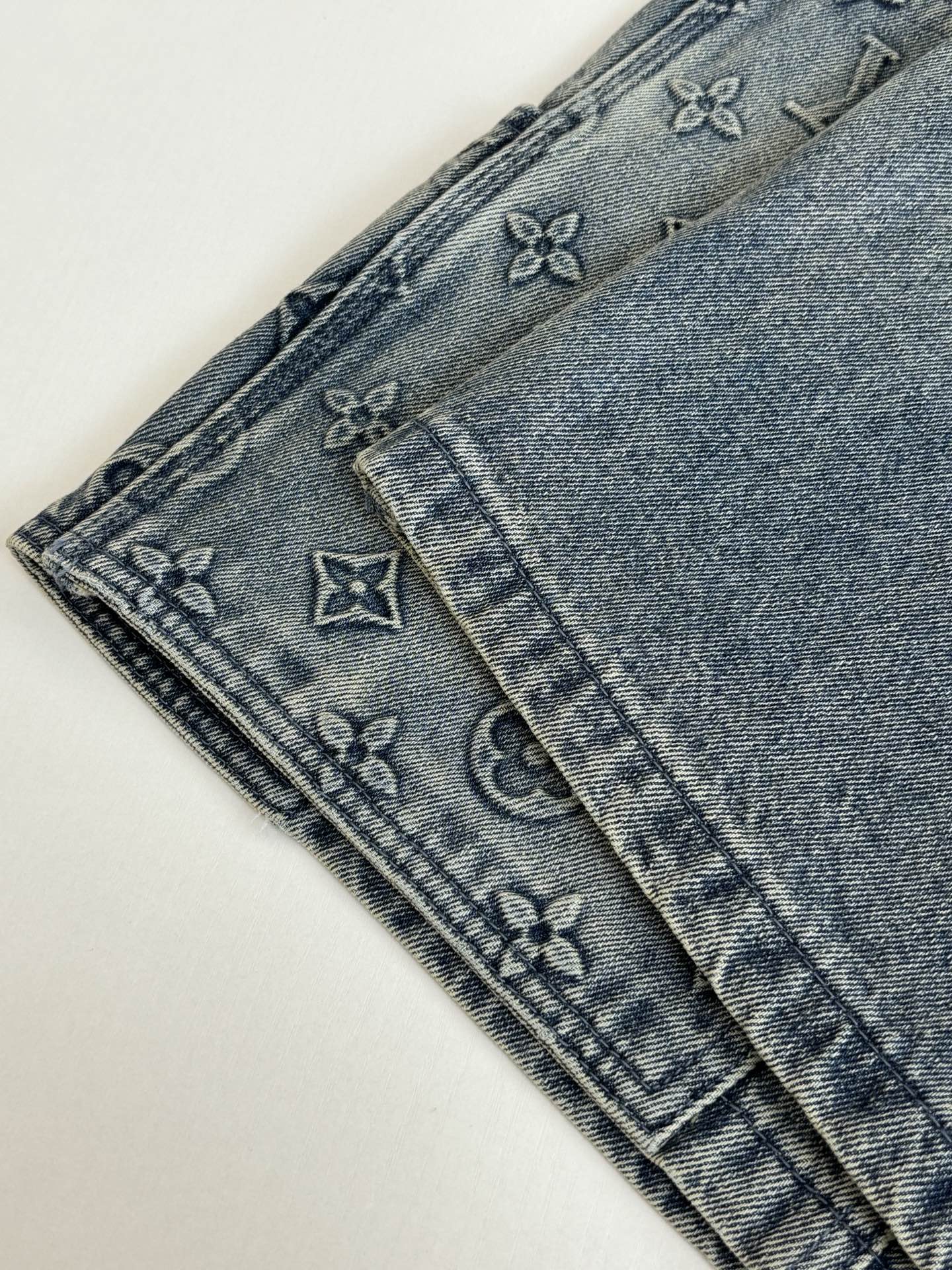 Denim shorts leg close-up with monogram-pattern stitching and belt loops