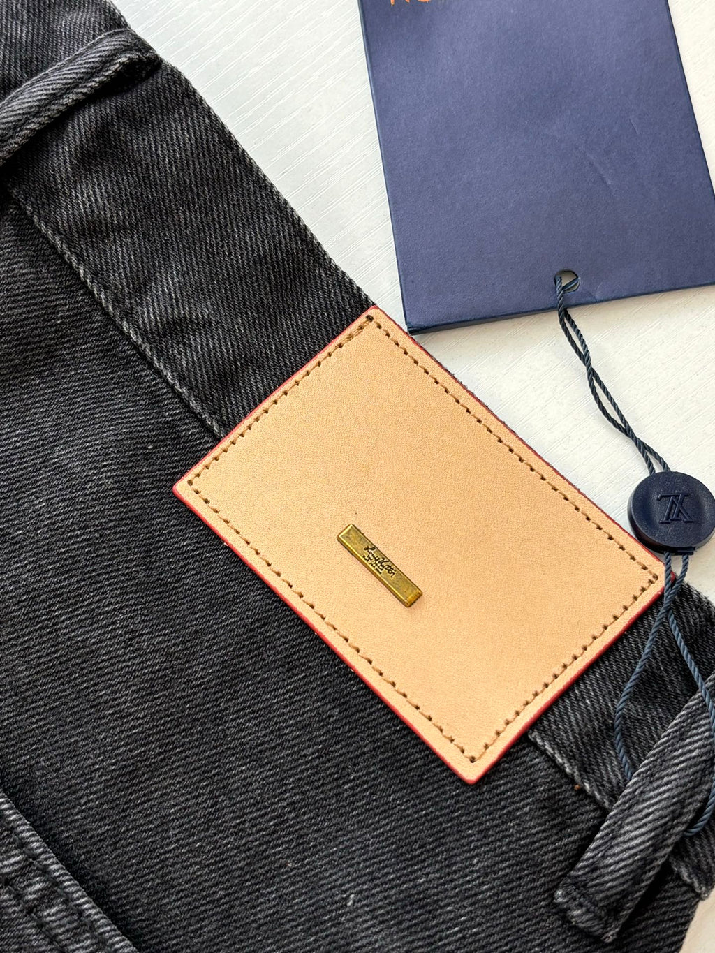 Brown leather Louis Vuitton tag and navy hang tag on dark denim shorts