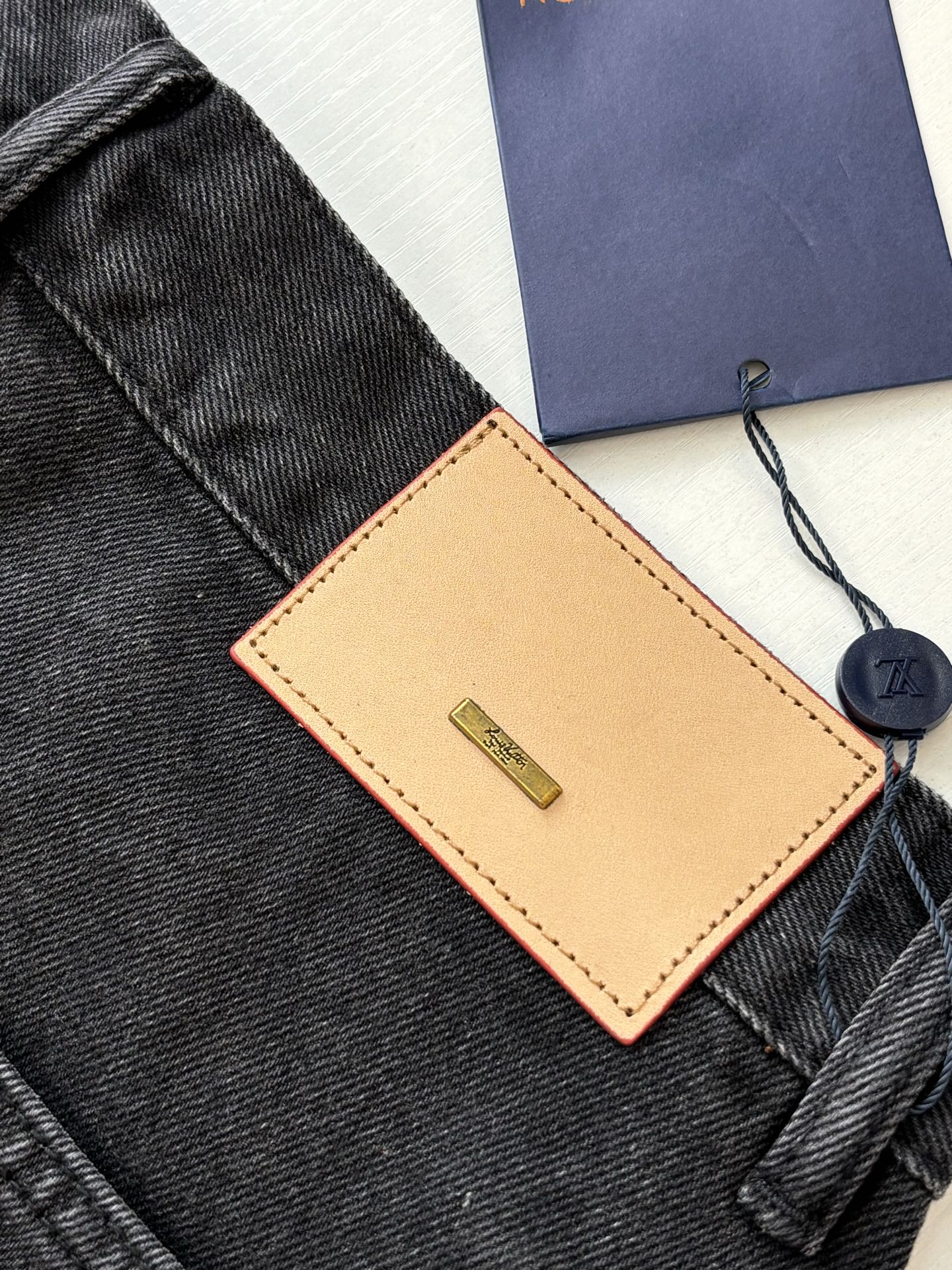 Brown leather Louis Vuitton tag and navy hang tag on dark denim shorts