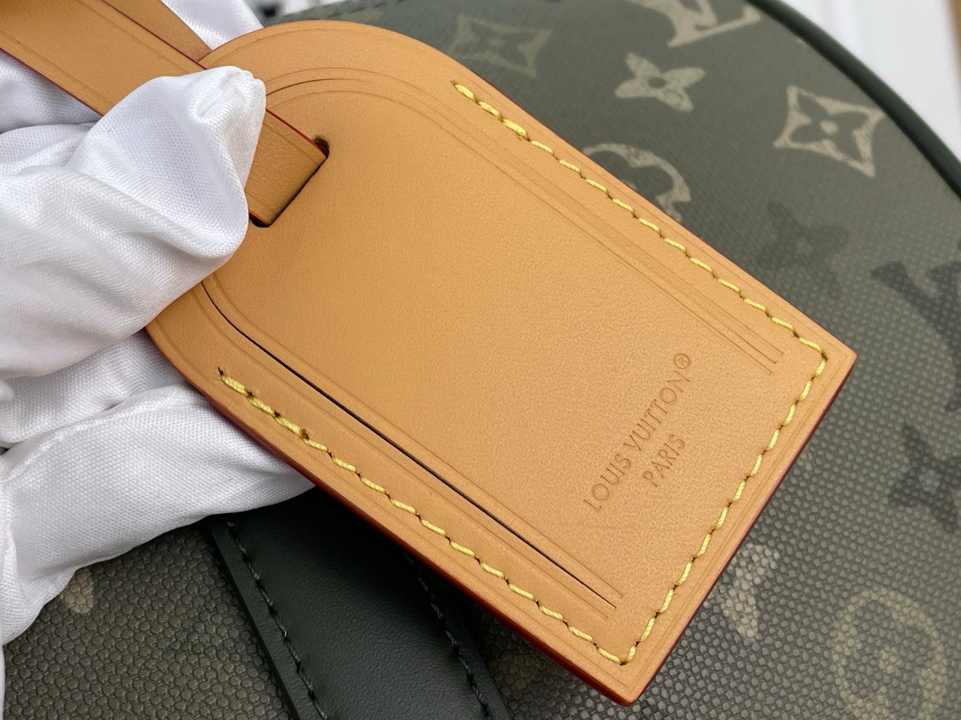 Louis Vuitton leather luggage tag in tan with gold stitching on dark green tote