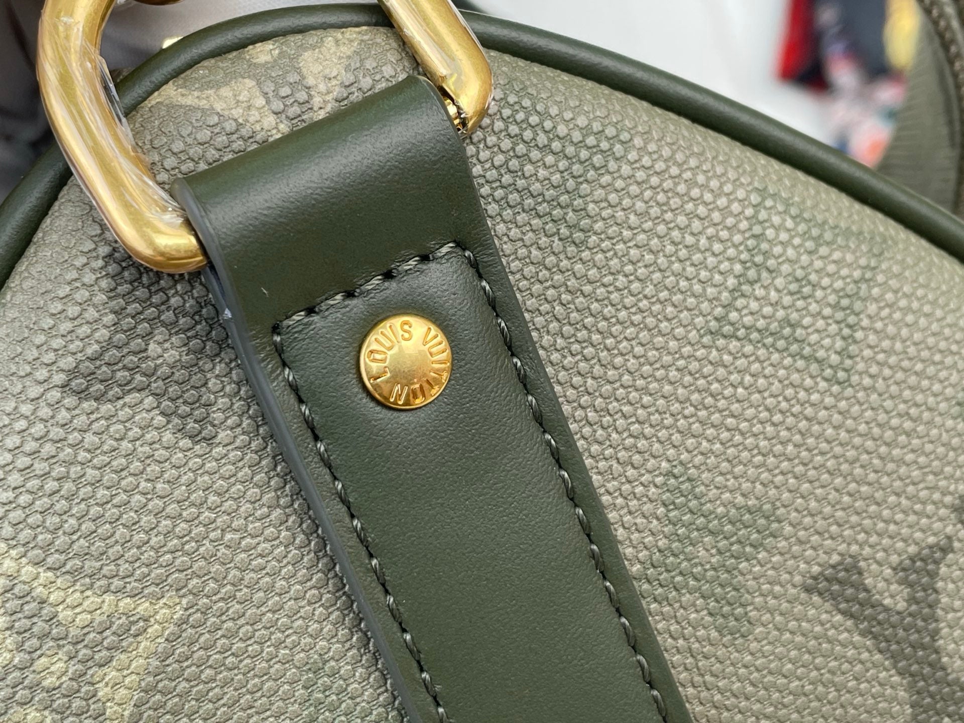 Louis Vuitton tote bag close-up: dark green textured leather strap with gold round logo