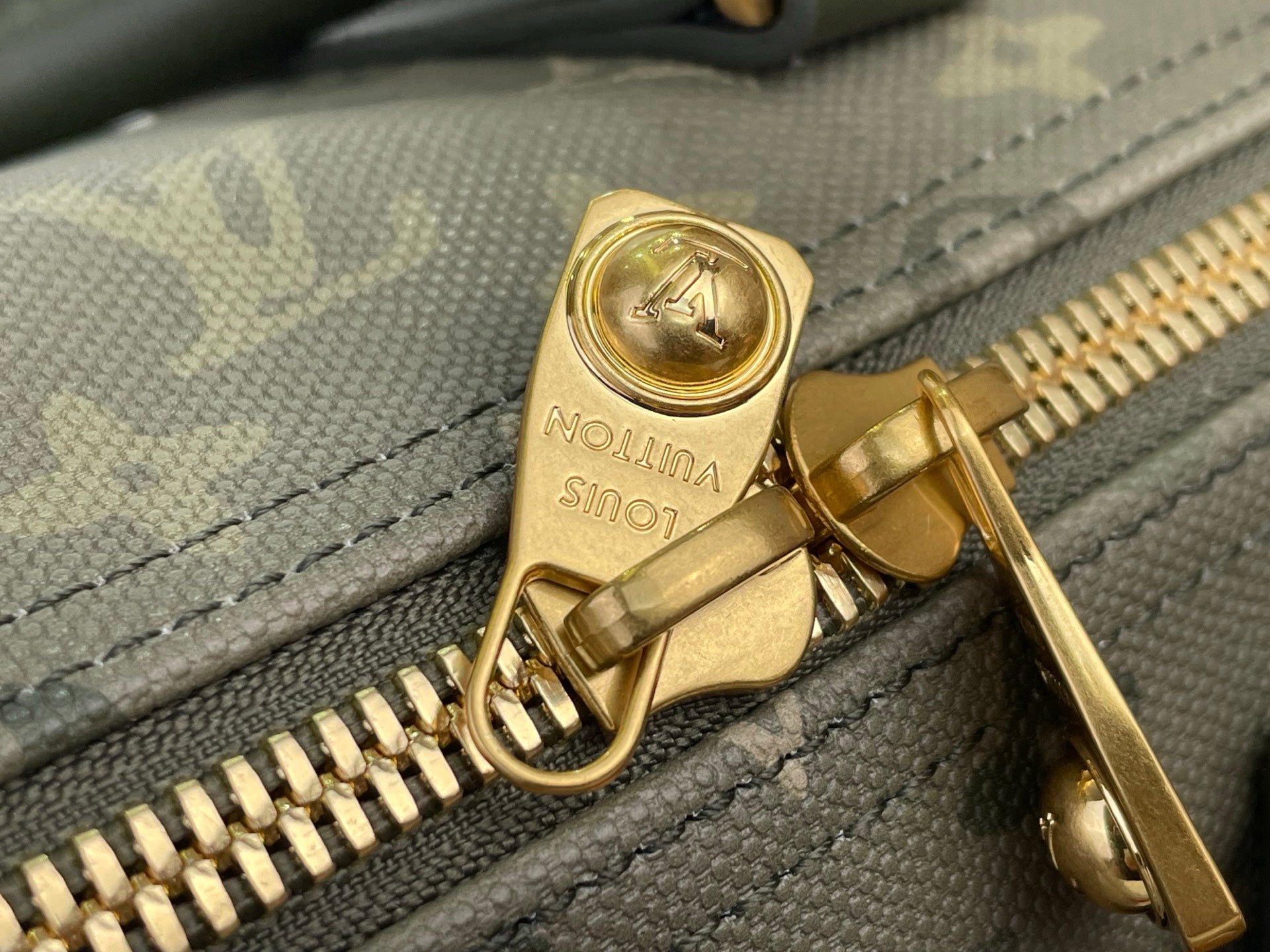 Louis Vuitton zipper pull and teeth close-up on dark green monogram fabric