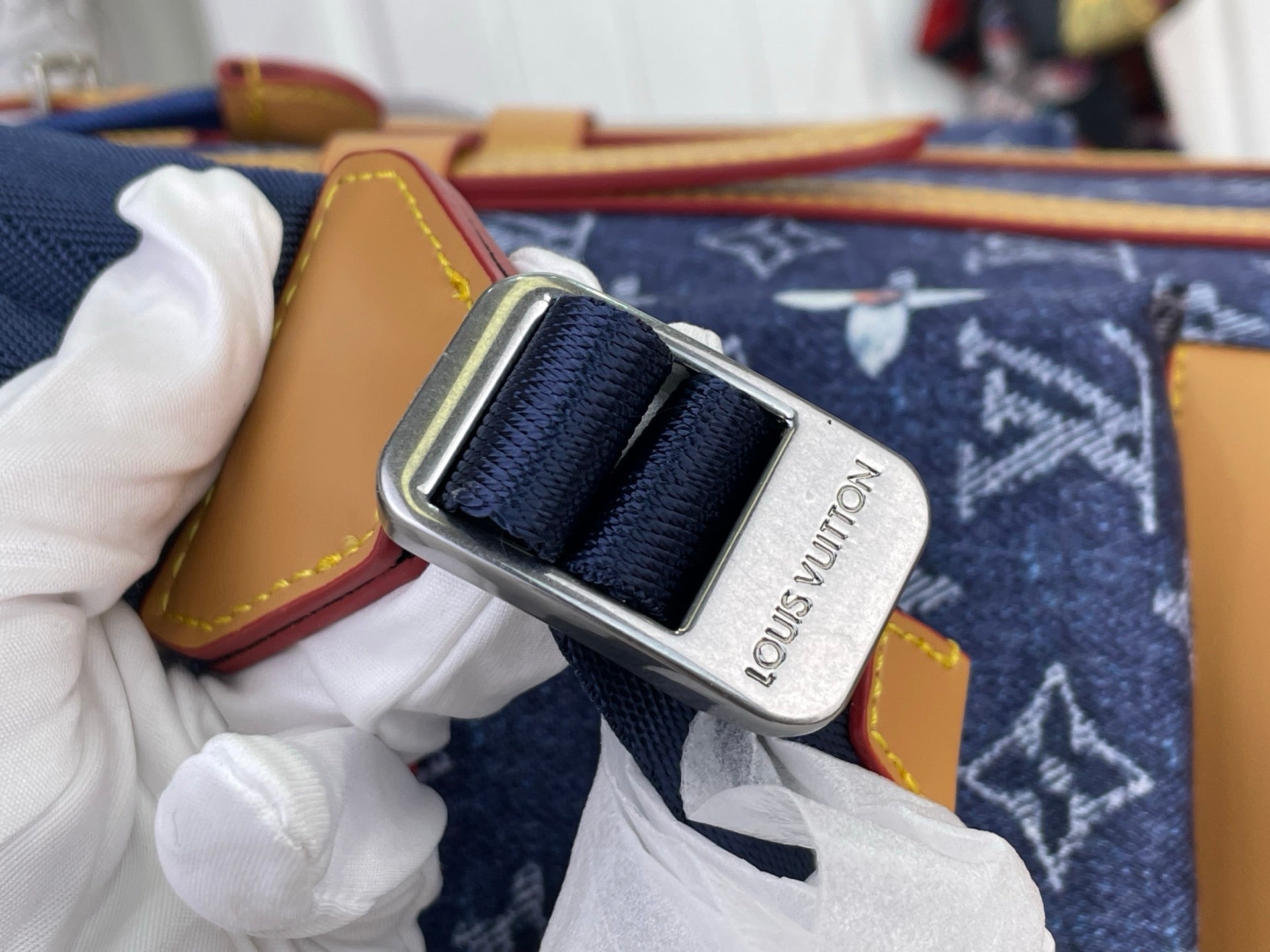 Louis Vuitton logo buckle securing dark blue strap on tan-trimmed monogram canvas