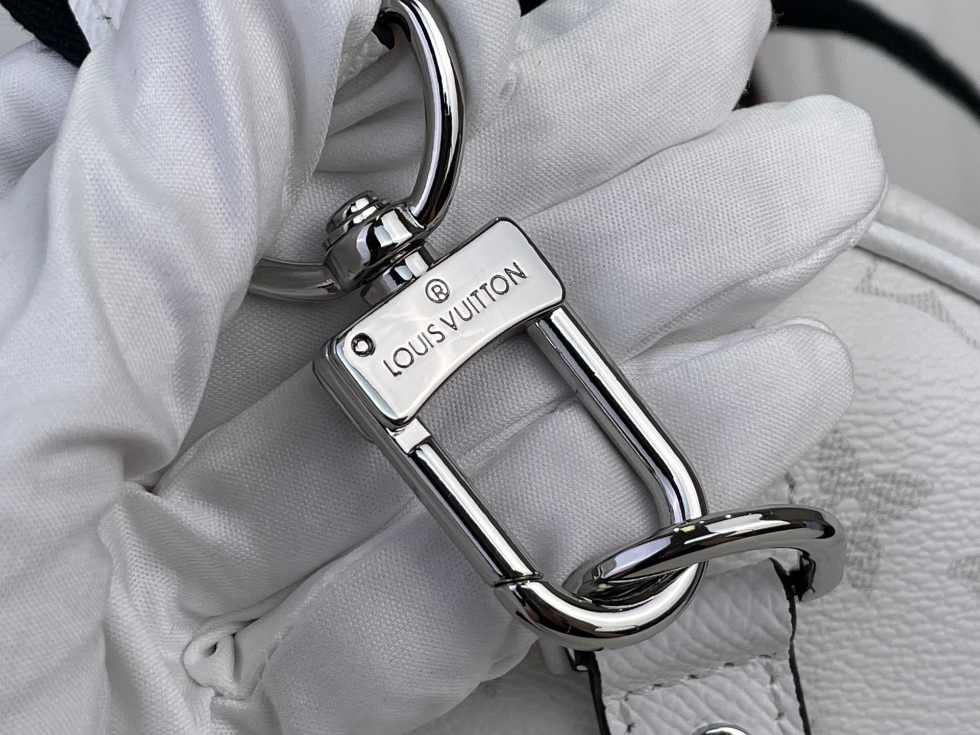 Close-up of Louis Vuitton logo keyring clasp and metal swivel hardware on bag