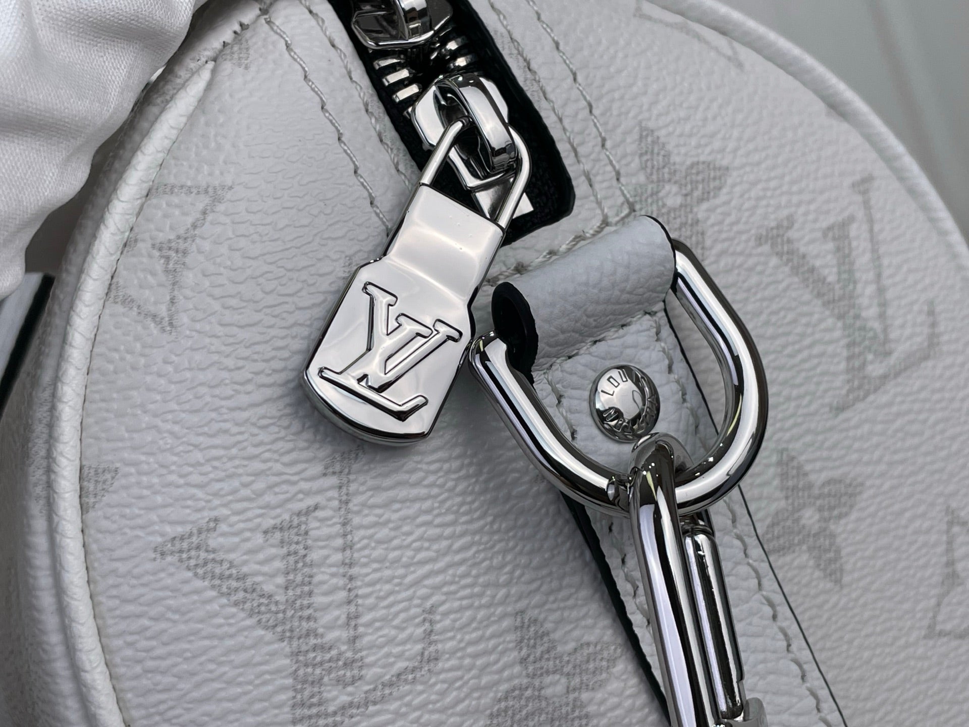 Close-up of white Louis Vuitton monogram bag hardware, D-rings, and keyring charm