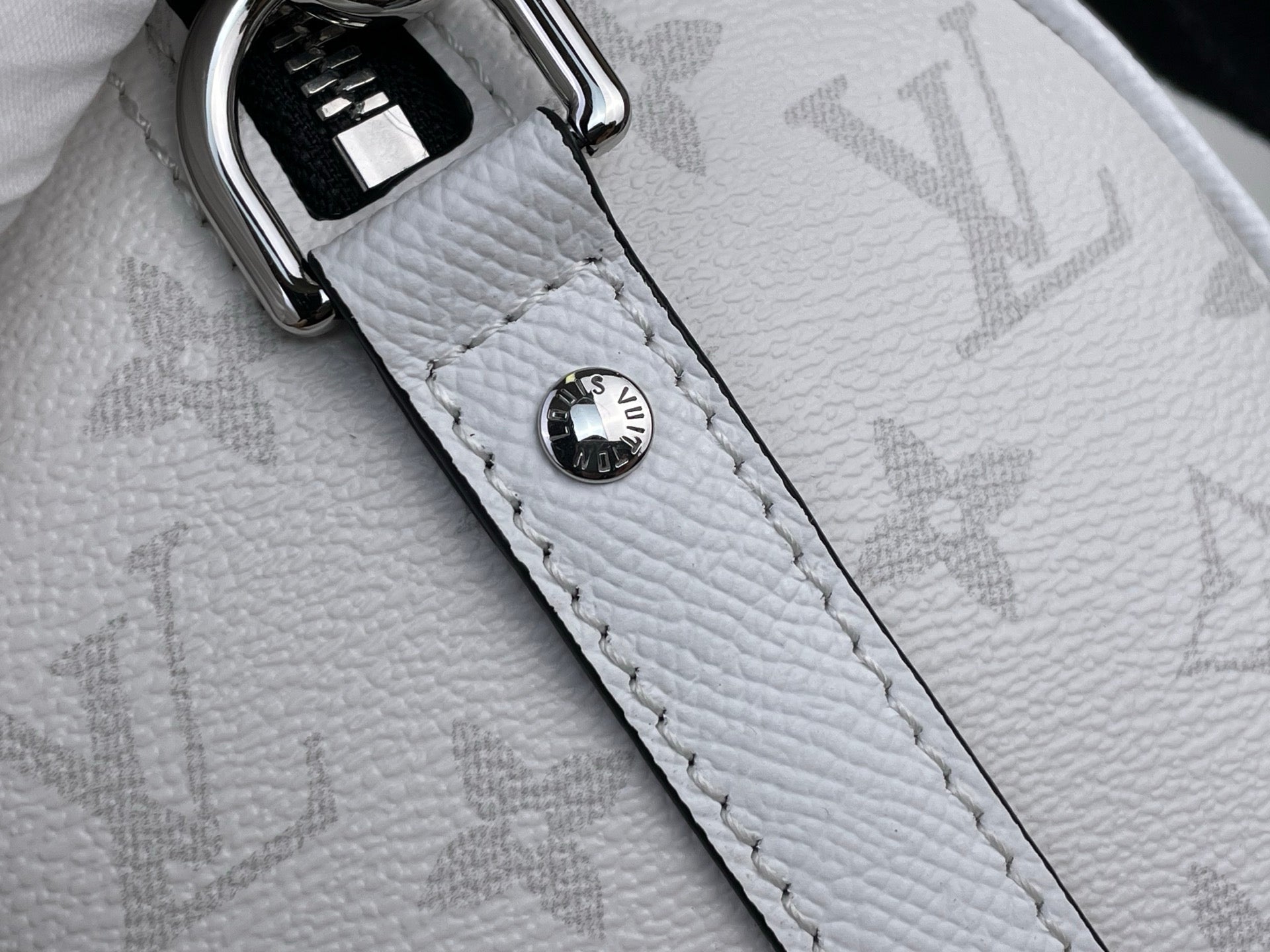 Close-up of white Louis Vuitton monogram bag strap with logo snap button
