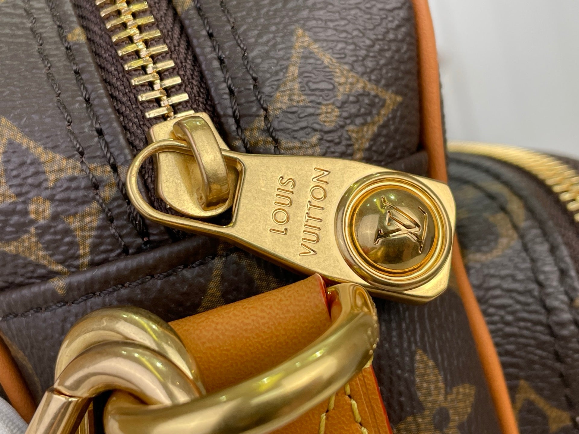 Louis Vuitton monogram bag clasp with gold-tone hardware and tan leather detail