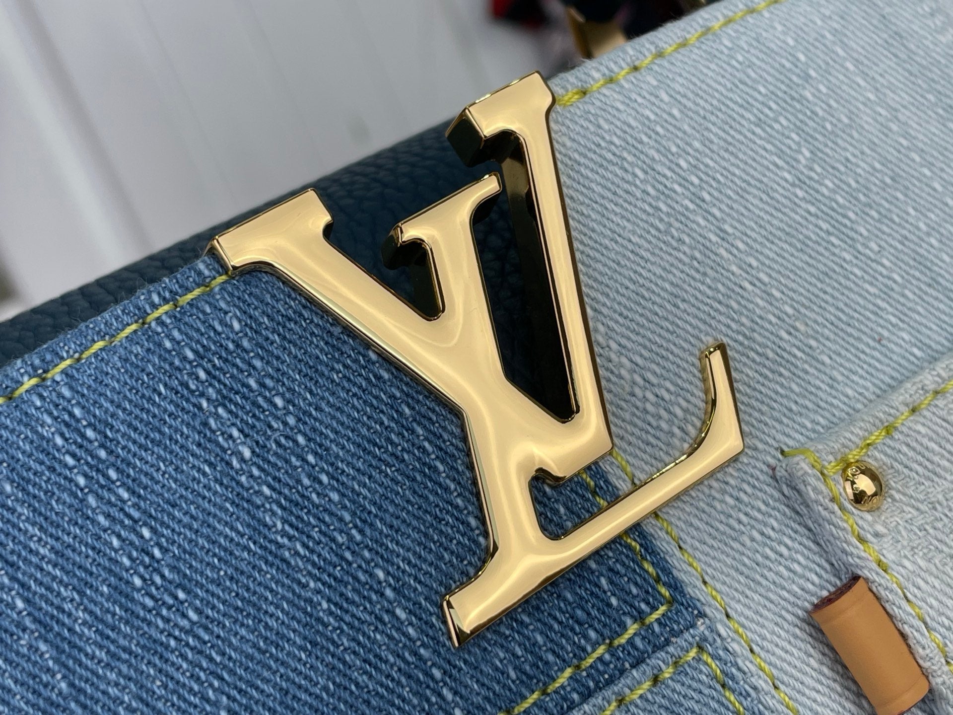 Gold LV logo plaque on blue denim-look leather panel with yellow stitching detail