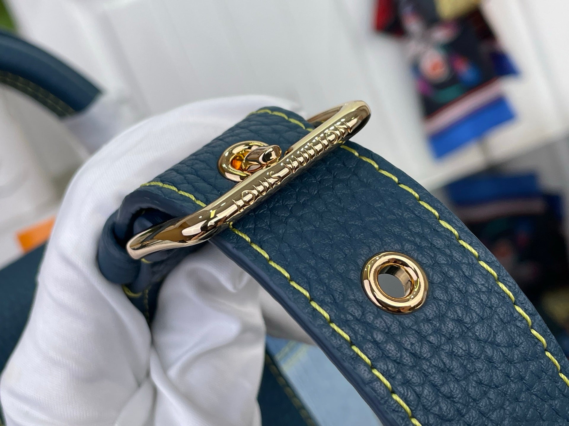 Gold ring hardware on blue textured leather strap with yellow edge stitching
