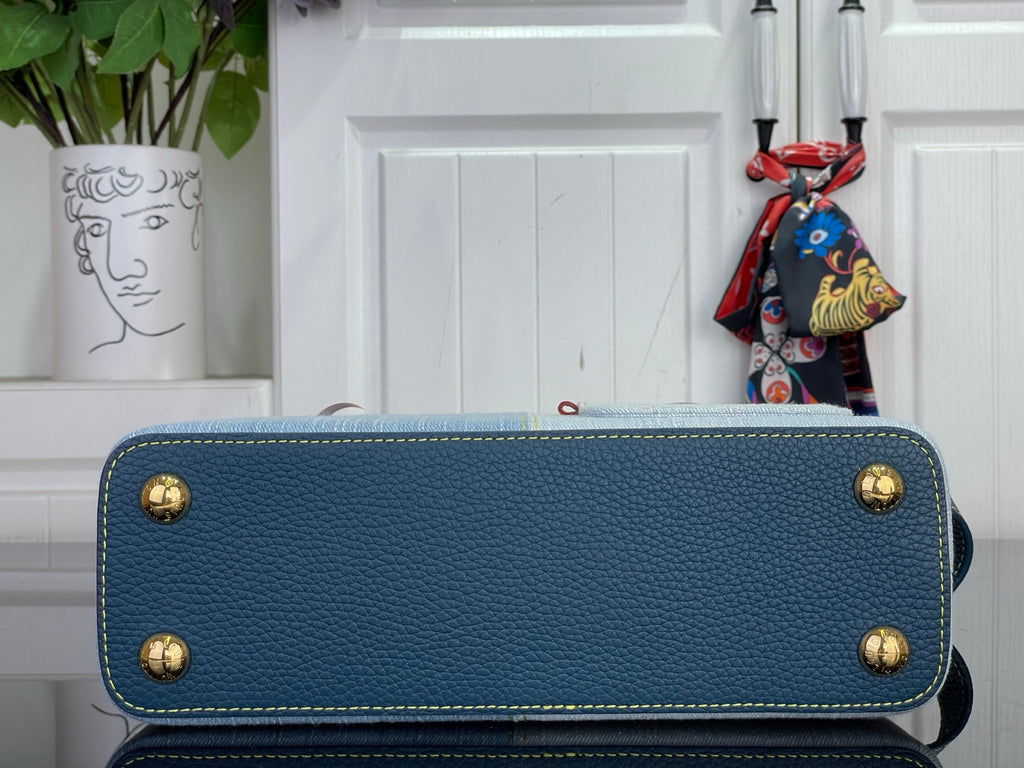 Blue textured handbag with gold corner studs and top handle, exterior close-up