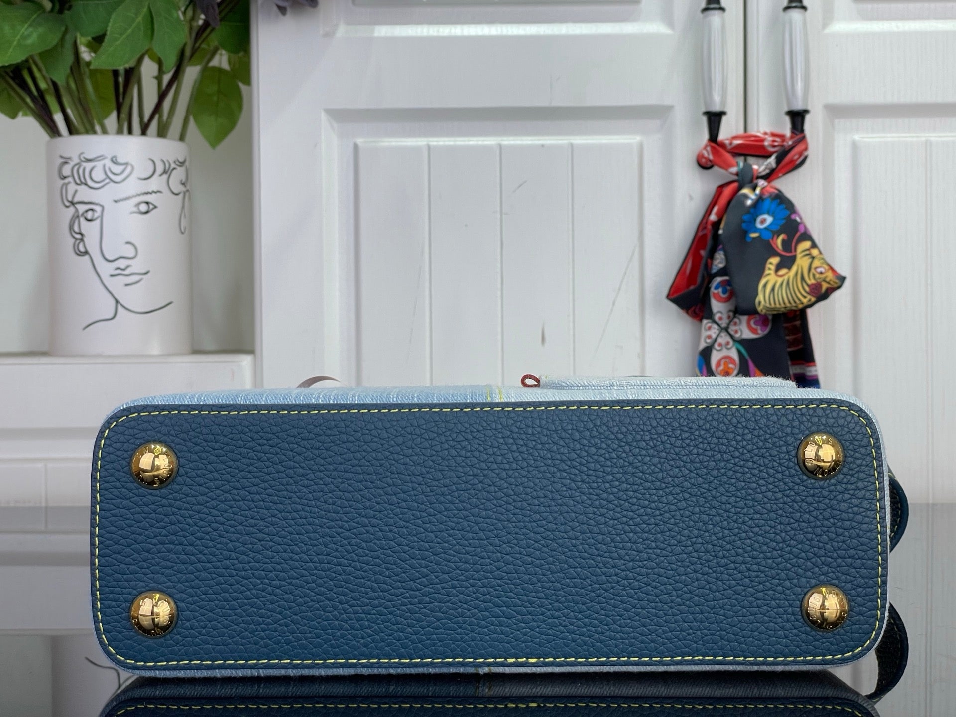 Blue textured handbag with gold corner studs and top handle, exterior close-up