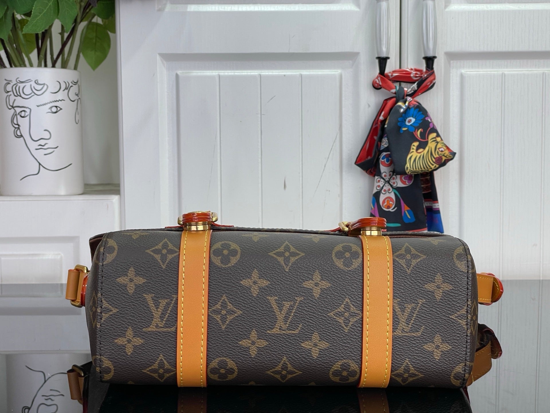 Monogram duffel-style bag with tan trim, top handles, and colorful scarf charm