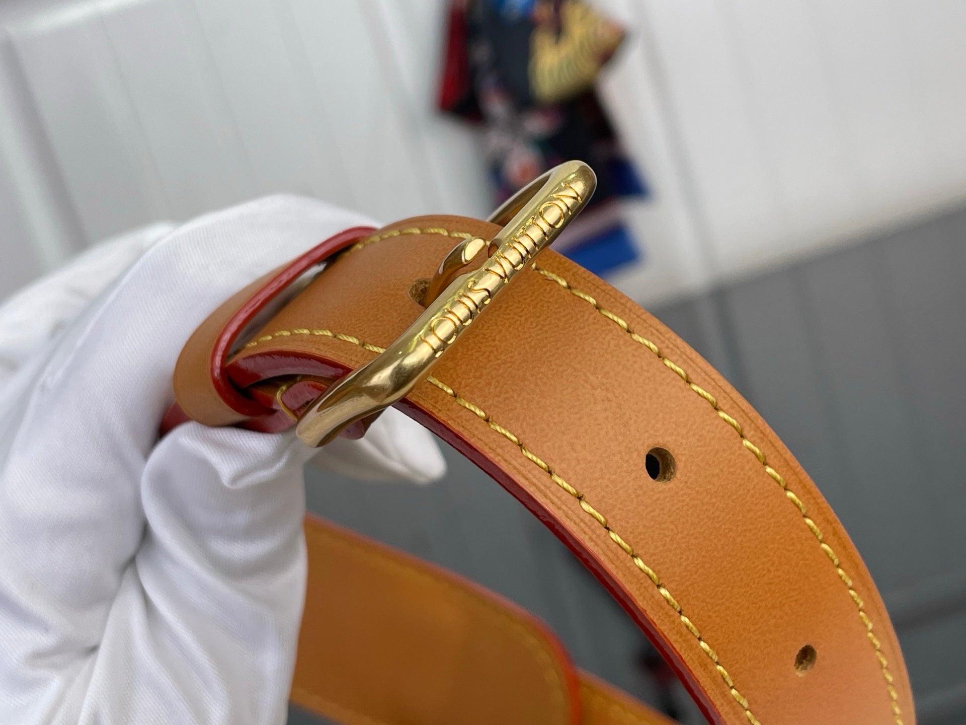 Tan leather strap detail with gold buckle hardware and stitching on monogram bag